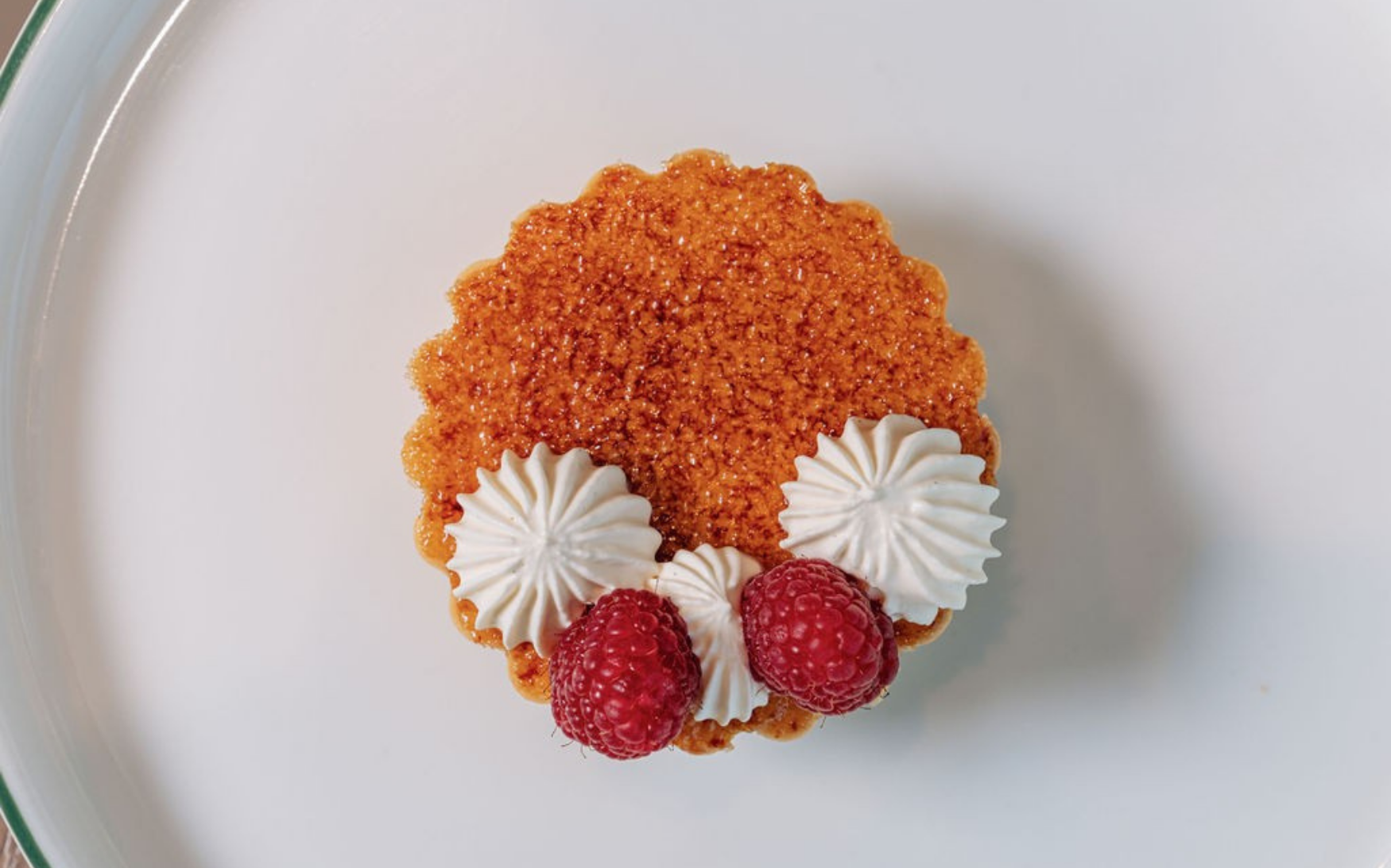 Small tart topped with raspberries and piped cream presented on a white plate.
