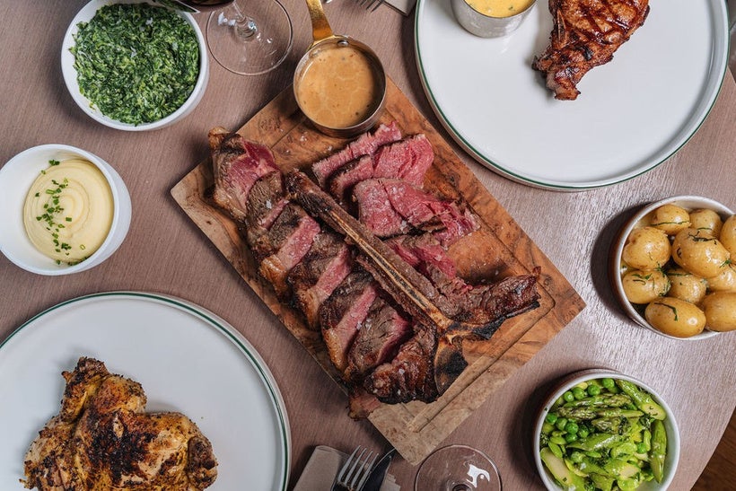 Overhead view of sliced grilled steak served with roasted potatoes, vegetables, and sauces.