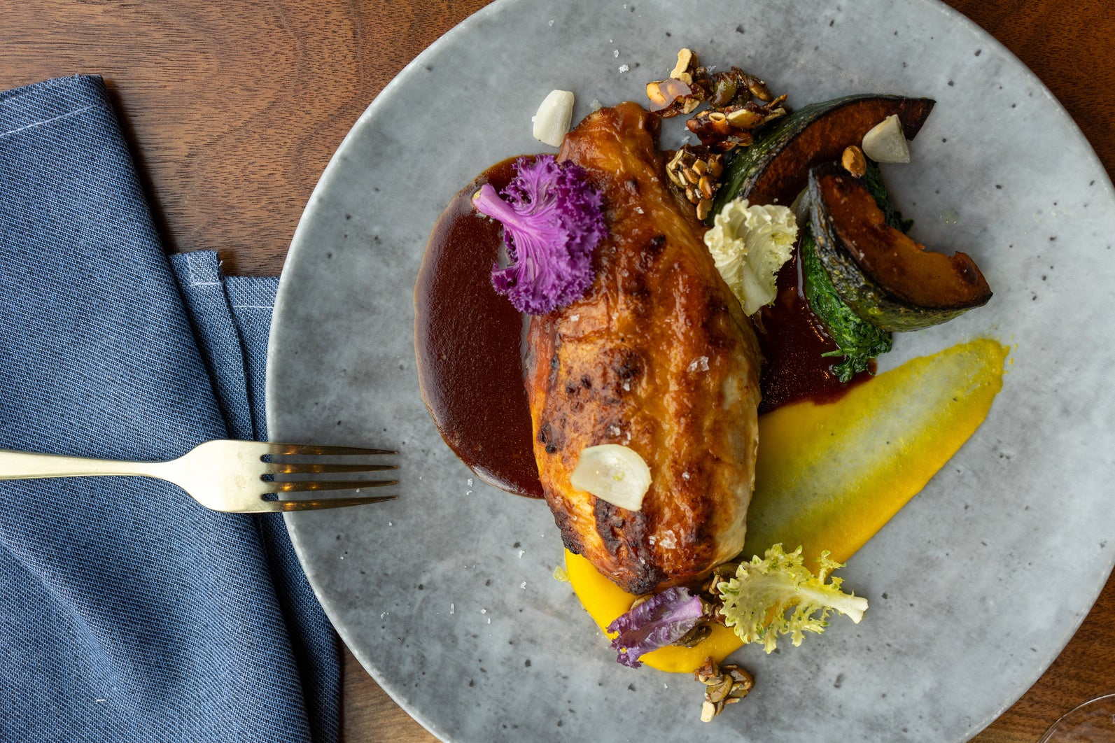 Roasted chicken breast on a ceramic plate served with roasted squash, gem lettuce, carrot purée, and toasted seeds.