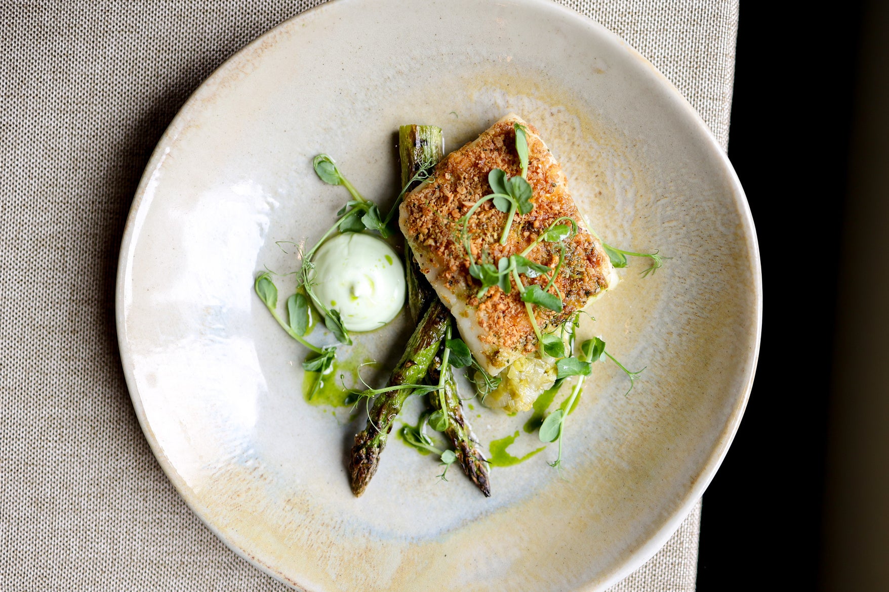 Pan-seared fish fillet with asparagus, cucumber, and creamy sauce served on a ceramic plate.